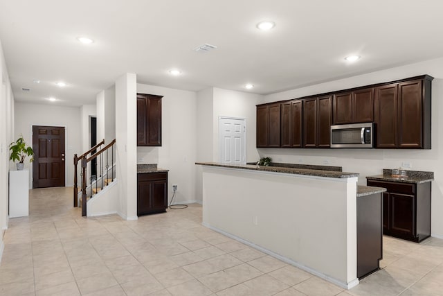 kitchen with dark brown cabinets, a kitchen island, dark stone counters, and light tile patterned flooring