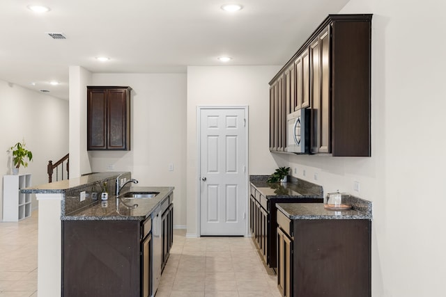 kitchen with light tile patterned floors, dark brown cabinetry, dark stone countertops, and sink