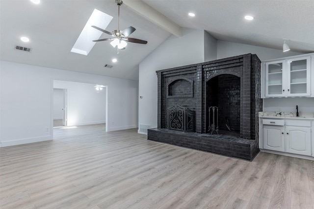 unfurnished living room with vaulted ceiling with skylight, ceiling fan, a fireplace, and light hardwood / wood-style flooring