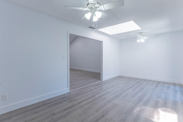 spare room with a skylight, ceiling fan, light hardwood / wood-style floors, and a textured ceiling