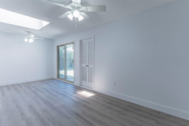 spare room with hardwood / wood-style flooring, ceiling fan, a textured ceiling, and a skylight