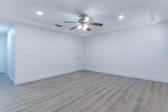 empty room featuring a raised ceiling, ceiling fan, a textured ceiling, and light wood-type flooring