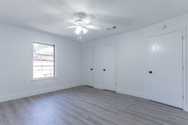 unfurnished bedroom with ceiling fan, light hardwood / wood-style floors, a textured ceiling, and multiple closets