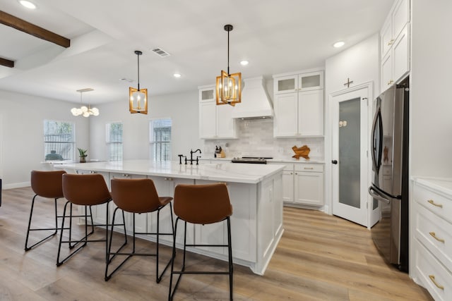 kitchen with visible vents, white cabinetry, freestanding refrigerator, decorative backsplash, and custom range hood