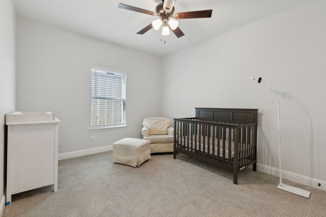 bedroom with light carpet, ceiling fan, a crib, and baseboards