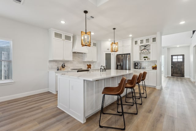 kitchen with visible vents, stainless steel fridge with ice dispenser, an island with sink, custom range hood, and white cabinetry