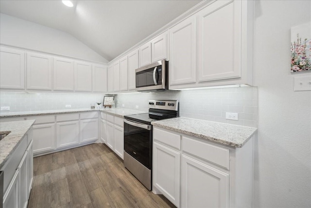 kitchen featuring light stone counters, white cabinetry, stainless steel appliances, and vaulted ceiling