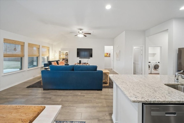 living room with washing machine and clothes dryer, ceiling fan, sink, and light wood-type flooring