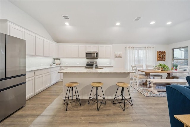 kitchen featuring a kitchen island with sink, a kitchen breakfast bar, light stone countertops, white cabinetry, and stainless steel appliances