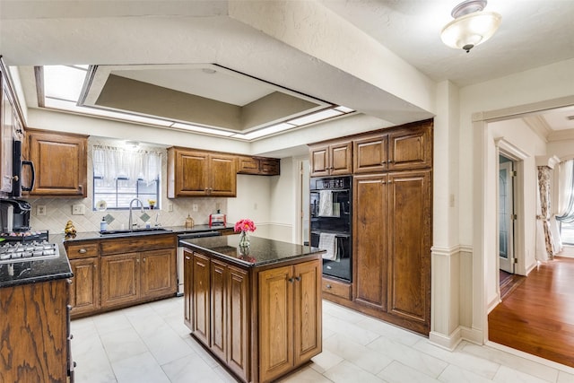 kitchen with decorative backsplash, dark stone counters, black appliances, sink, and a center island