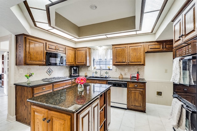 kitchen with dark stone counters, stainless steel gas cooktop, sink, dishwasher, and a center island