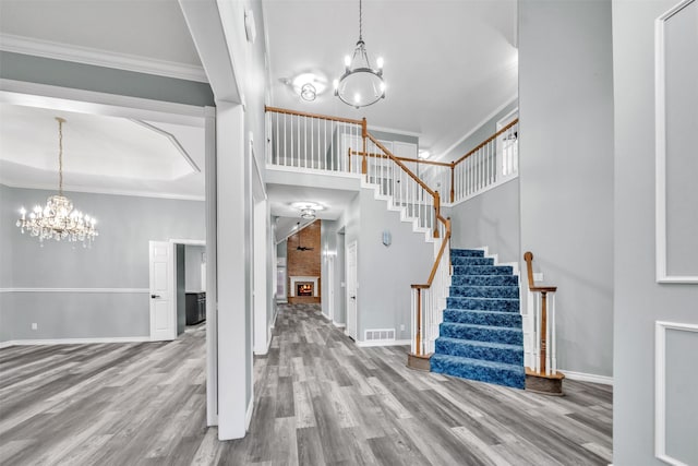 entryway featuring a large fireplace, a high ceiling, a notable chandelier, crown molding, and hardwood / wood-style flooring