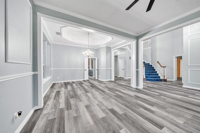 unfurnished living room featuring a raised ceiling, crown molding, and ceiling fan with notable chandelier