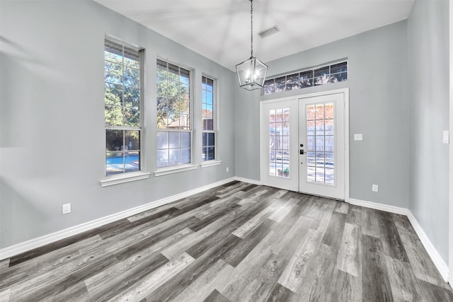 unfurnished dining area with a healthy amount of sunlight, french doors, wood-type flooring, and a notable chandelier