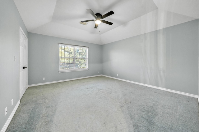 empty room featuring ceiling fan, vaulted ceiling, carpet floors, and a tray ceiling