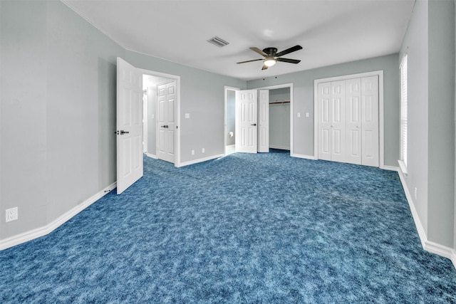 unfurnished bedroom featuring multiple closets, ceiling fan, and dark carpet