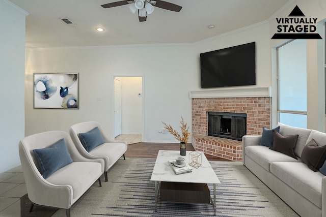 living room with tile patterned flooring, a brick fireplace, ornamental molding, and ceiling fan