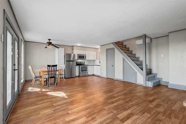 unfurnished living room featuring a wall mounted air conditioner, french doors, light wood-type flooring, a wealth of natural light, and ceiling fan