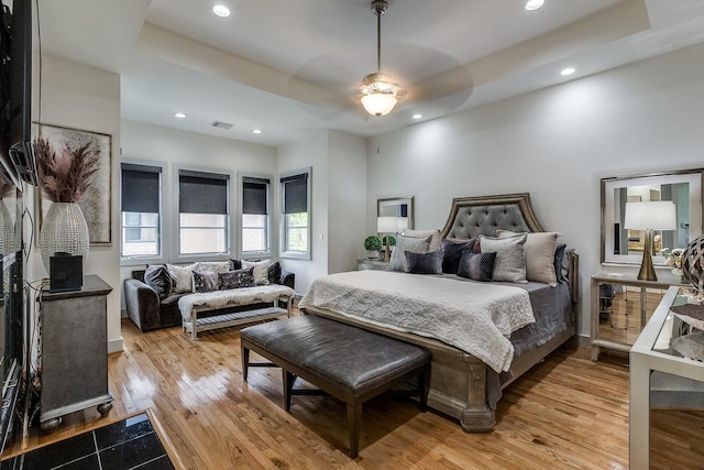 bedroom with ceiling fan, light wood-type flooring, and a tray ceiling