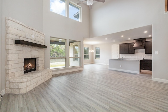 unfurnished living room with a towering ceiling, ceiling fan, sink, light hardwood / wood-style floors, and a stone fireplace