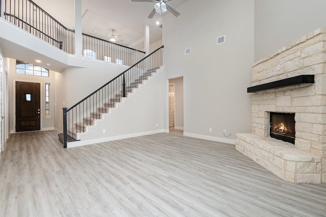 unfurnished living room with ceiling fan, a fireplace, a towering ceiling, and light wood-type flooring