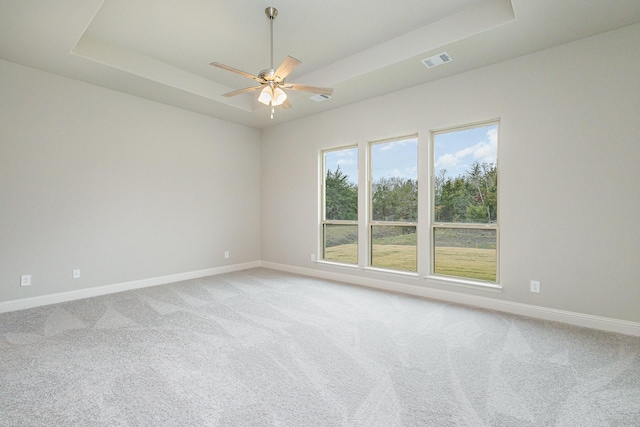 empty room with ceiling fan, light colored carpet, and a tray ceiling