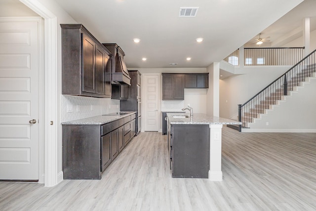 kitchen featuring light stone countertops, ceiling fan, a kitchen island with sink, and light hardwood / wood-style floors