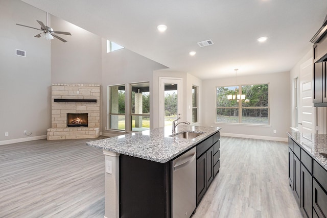 kitchen featuring dishwasher, sink, hanging light fixtures, a stone fireplace, and a center island with sink