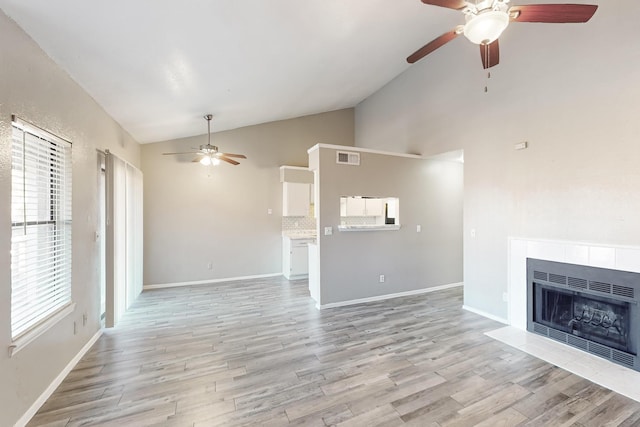 unfurnished living room featuring a tiled fireplace, vaulted ceiling, light hardwood / wood-style floors, and ceiling fan