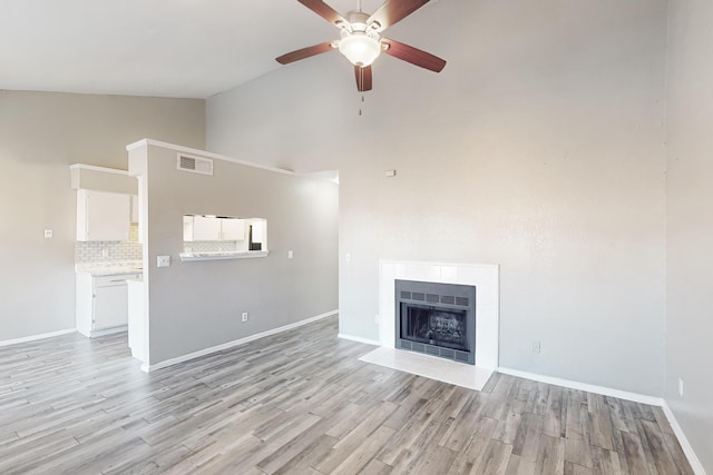 unfurnished living room featuring ceiling fan, high vaulted ceiling, a tile fireplace, and light wood-type flooring