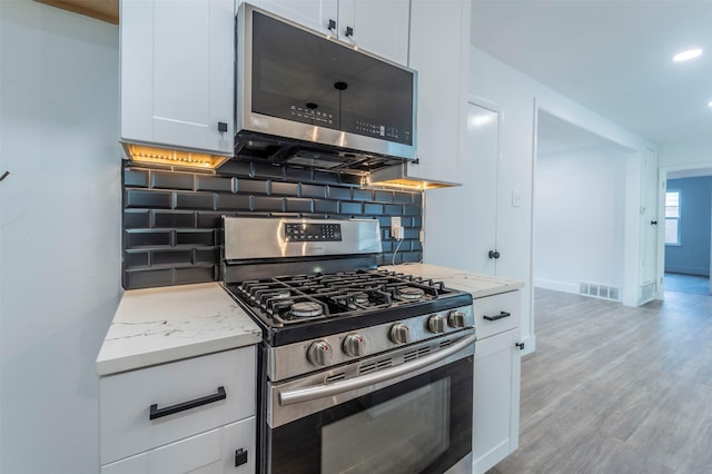 kitchen with light stone countertops, white cabinetry, light hardwood / wood-style flooring, and stainless steel appliances