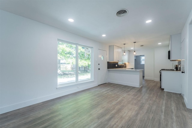 kitchen with kitchen peninsula, sink, wood-type flooring, decorative light fixtures, and white cabinetry