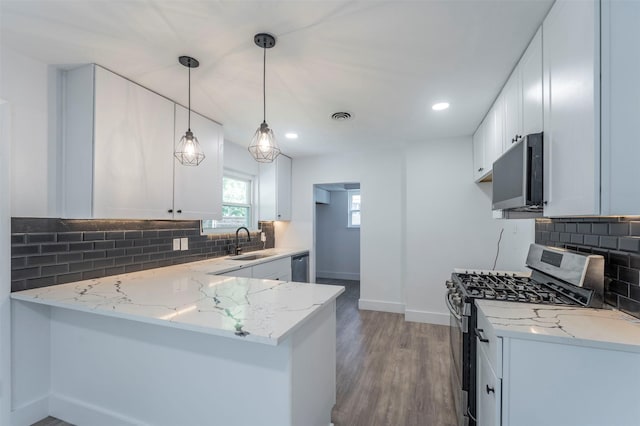 kitchen with sink, kitchen peninsula, decorative light fixtures, white cabinets, and appliances with stainless steel finishes