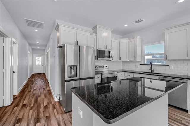 kitchen featuring stainless steel appliances, sink, dark stone countertops, a center island, and white cabinetry