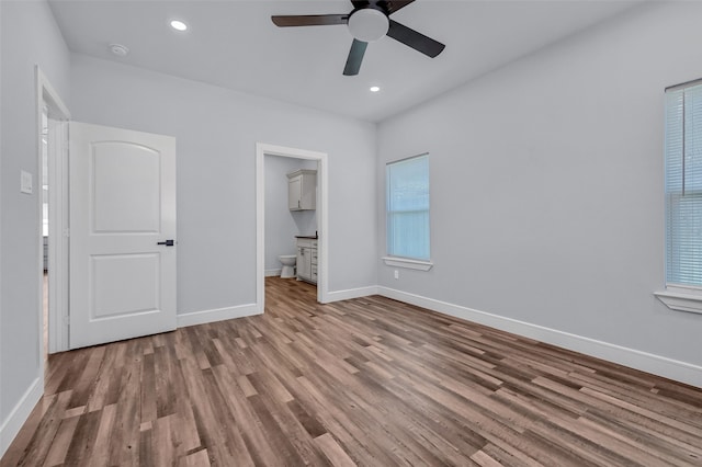 unfurnished bedroom featuring ceiling fan, light hardwood / wood-style floors, a walk in closet, and ensuite bath