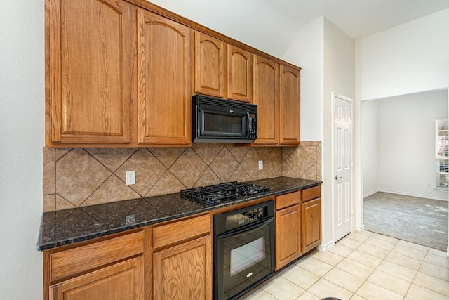 kitchen with dark stone countertops, light tile patterned floors, decorative backsplash, and black appliances