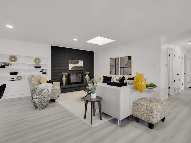 living room with a brick fireplace, a skylight, built in features, and light wood-type flooring