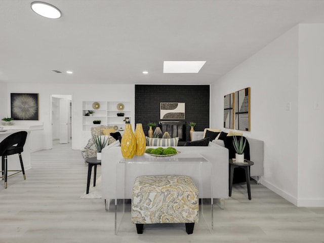 living room featuring built in features, a skylight, a brick fireplace, and light hardwood / wood-style flooring