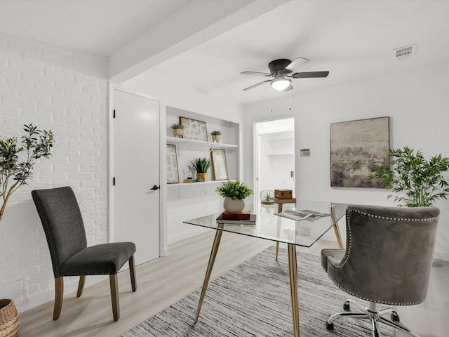 home office featuring light hardwood / wood-style flooring, ceiling fan, and brick wall