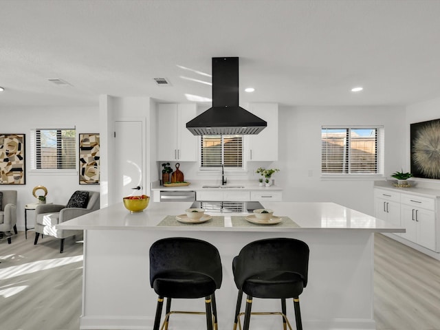 kitchen featuring a breakfast bar area, light wood-type flooring, a kitchen island, island exhaust hood, and white cabinets