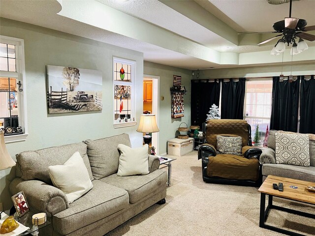 carpeted living room with ceiling fan and a tray ceiling