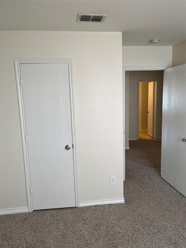 unfurnished bedroom with dark colored carpet and a closet