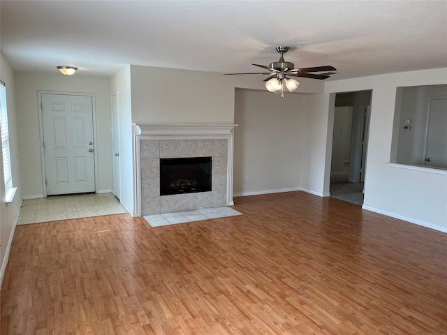 unfurnished living room featuring wood-type flooring, ceiling fan, and a tiled fireplace