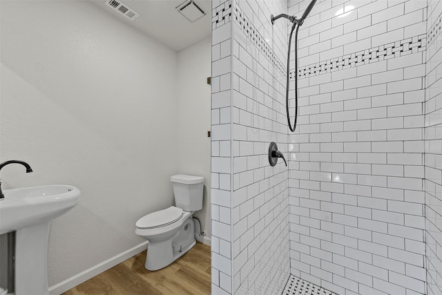 bathroom with toilet, tiled shower, wood finished floors, and visible vents