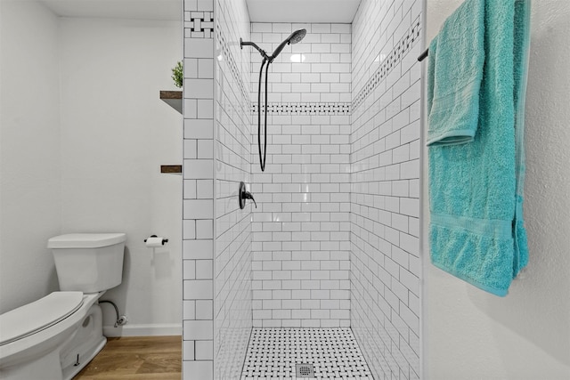 full bath featuring toilet, baseboards, tiled shower, and wood finished floors