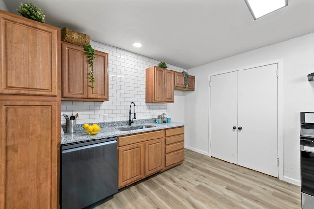 kitchen featuring dishwashing machine, a sink, backsplash, light wood finished floors, and brown cabinetry