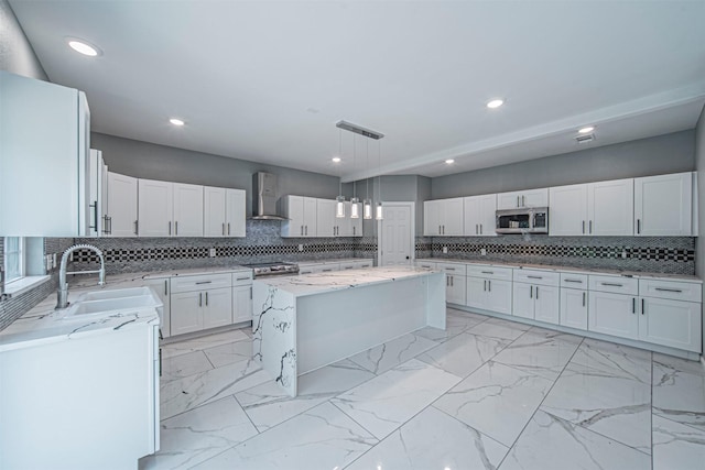 kitchen featuring sink, white cabinets, a center island, stainless steel appliances, and wall chimney range hood