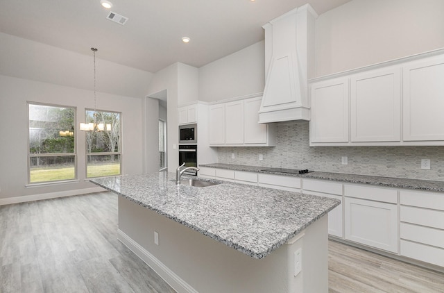 kitchen with white cabinetry, sink, oven, and a kitchen island with sink