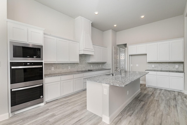 kitchen with white cabinets, black electric cooktop, light stone counters, and a kitchen island with sink