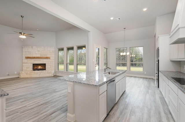 kitchen with dishwasher, white cabinetry, a kitchen island with sink, and a stone fireplace